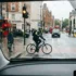 Learner driver approaching a cyclist and pedestrian at a rainy London crossing, illustrating hazard perception and driver awareness
